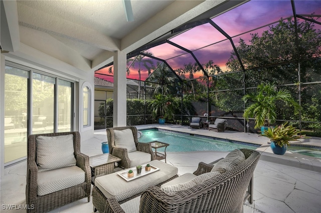 pool at dusk with glass enclosure, a patio, and an outdoor living space