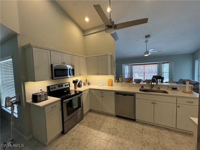 kitchen with kitchen peninsula, appliances with stainless steel finishes, ceiling fan, sink, and high vaulted ceiling