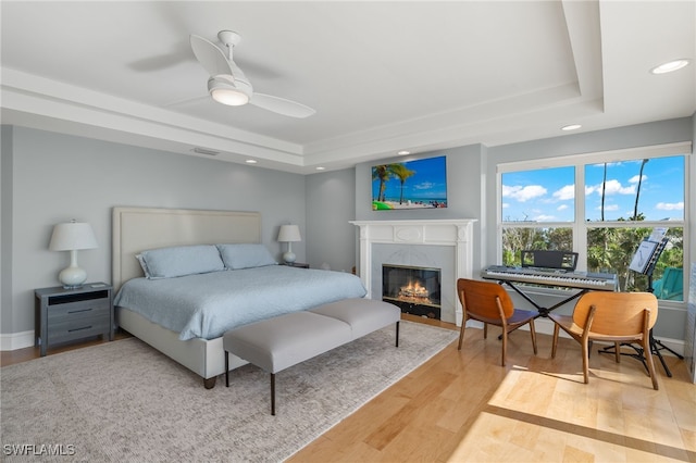 bedroom with a tray ceiling, ceiling fan, a premium fireplace, and hardwood / wood-style flooring