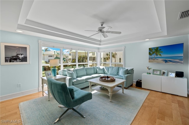 living room featuring a healthy amount of sunlight, light hardwood / wood-style flooring, and a tray ceiling