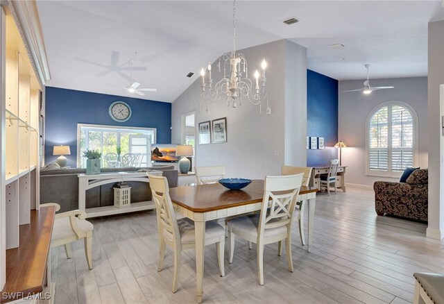 dining space featuring ceiling fan with notable chandelier, light wood-type flooring, and lofted ceiling