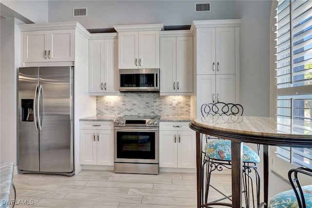 kitchen featuring white cabinets, decorative backsplash, light stone counters, and appliances with stainless steel finishes