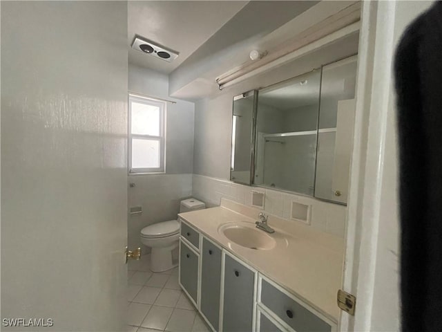 bathroom featuring tile patterned flooring, tile walls, vanity, a shower with shower door, and toilet