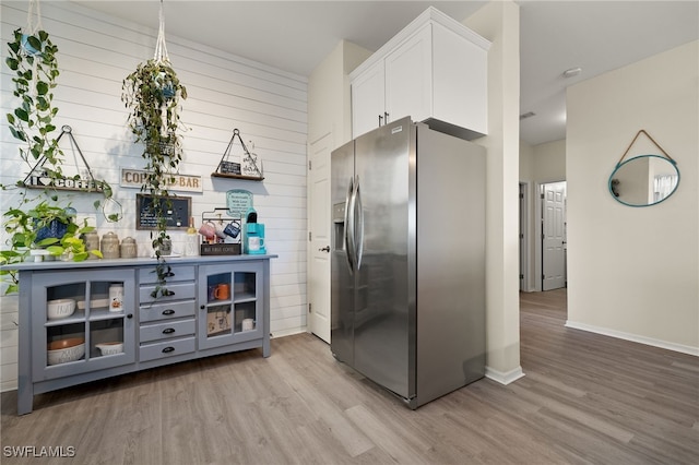 kitchen with stainless steel fridge, light hardwood / wood-style floors, white cabinetry, and wooden walls