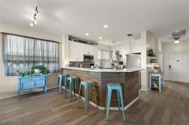 kitchen featuring white cabinetry, dark hardwood / wood-style floors, kitchen peninsula, a breakfast bar area, and decorative backsplash