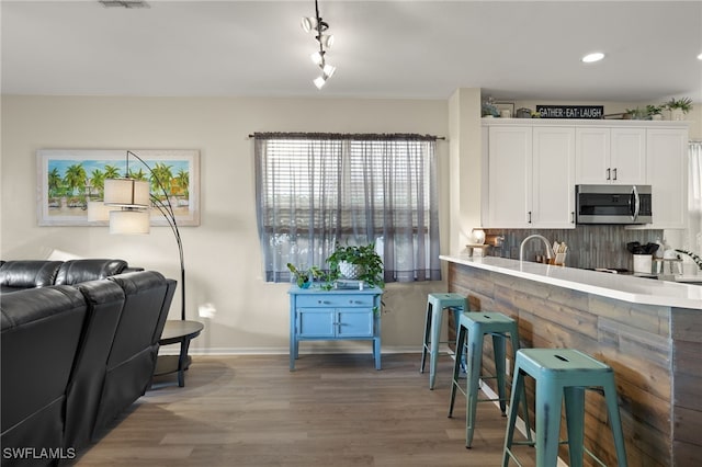 kitchen featuring decorative backsplash, white cabinetry, rail lighting, and hardwood / wood-style flooring