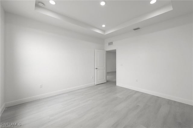 empty room featuring a raised ceiling and light hardwood / wood-style flooring