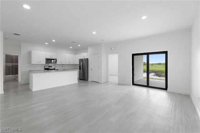 kitchen with a kitchen island with sink, white cabinets, sink, light hardwood / wood-style flooring, and stainless steel appliances