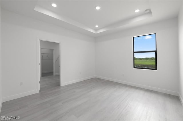 spare room with a tray ceiling and light hardwood / wood-style flooring