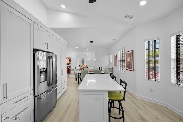 kitchen with light hardwood / wood-style flooring, stainless steel fridge, a kitchen island, white cabinets, and a kitchen bar