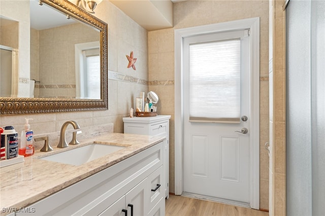 bathroom with vanity, a shower with door, decorative backsplash, tile walls, and wood-type flooring