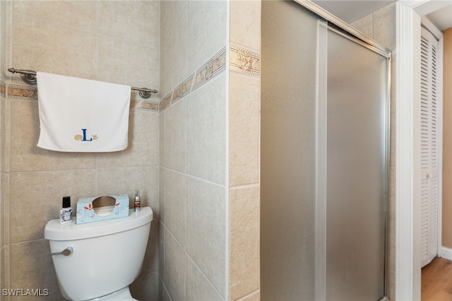 bathroom with a shower with door, tile walls, and toilet