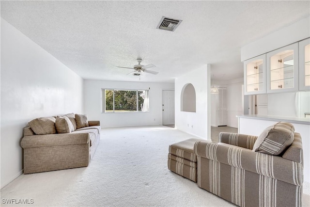 living room with ceiling fan, light carpet, and a textured ceiling