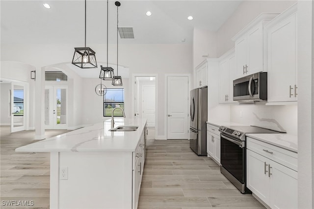 kitchen with stainless steel appliances, sink, decorative light fixtures, a center island with sink, and white cabinetry