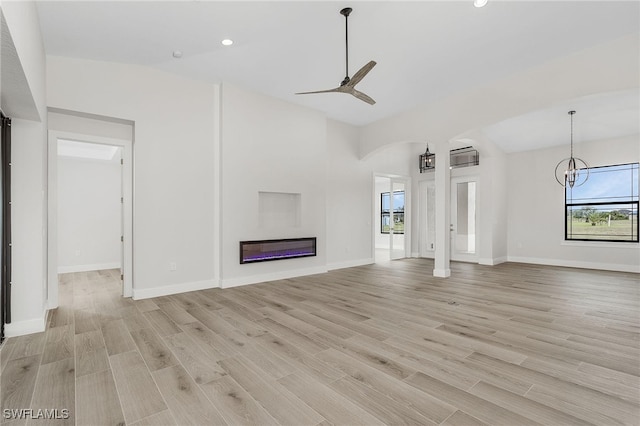 unfurnished living room with ceiling fan with notable chandelier and light wood-type flooring