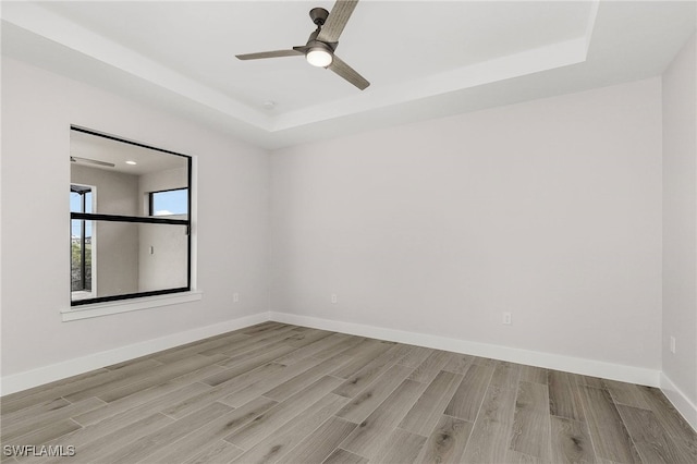 unfurnished room with light wood-type flooring, a raised ceiling, and ceiling fan