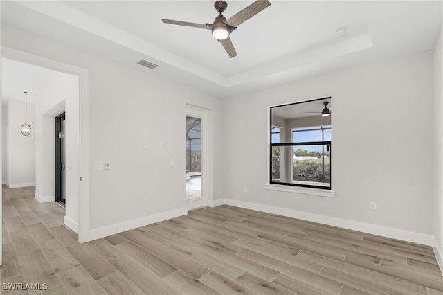 unfurnished room featuring a tray ceiling, ceiling fan, and light hardwood / wood-style flooring