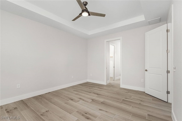 spare room with light hardwood / wood-style floors, ceiling fan, and a tray ceiling