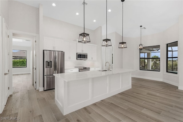 kitchen featuring a kitchen island with sink, white cabinets, sink, hanging light fixtures, and appliances with stainless steel finishes