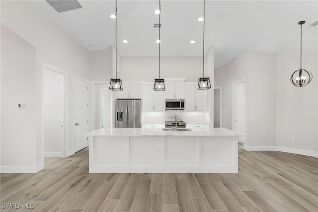 kitchen with light wood-type flooring, stainless steel appliances, a spacious island, decorative light fixtures, and white cabinets