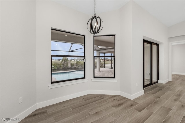 unfurnished dining area with lofted ceiling, wood-type flooring, and an inviting chandelier