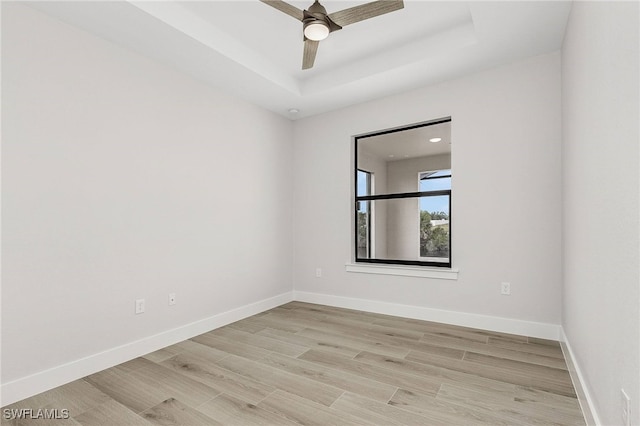 unfurnished room featuring ceiling fan, light wood-type flooring, and a tray ceiling