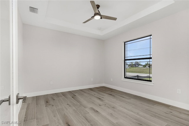 unfurnished room with a raised ceiling, ceiling fan, and light hardwood / wood-style floors