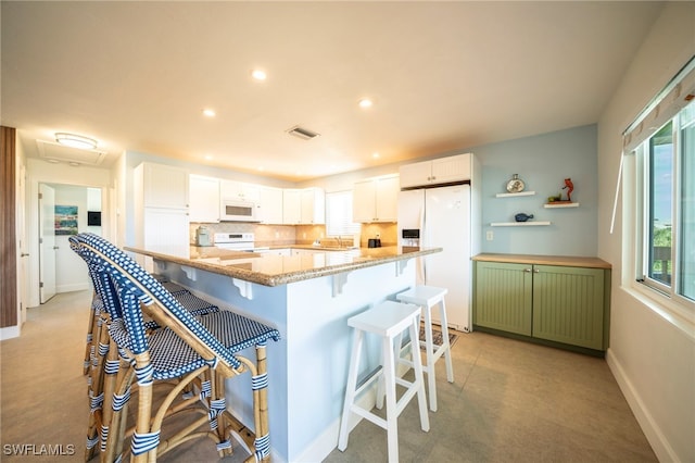 kitchen featuring white cabinets, a kitchen bar, white appliances, and plenty of natural light