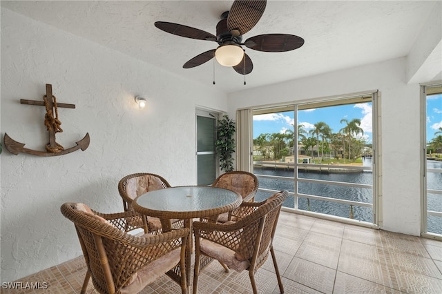 dining area featuring ceiling fan, light tile patterned floors, a water view, and a textured ceiling