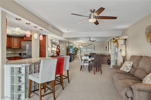 kitchen featuring ceiling fan, stainless steel refrigerator with ice dispenser, pendant lighting, light carpet, and a breakfast bar