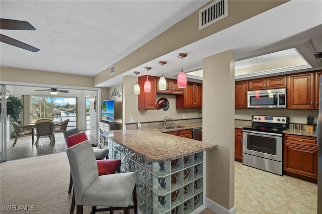 kitchen with kitchen peninsula, a kitchen bar, stainless steel appliances, sink, and hanging light fixtures