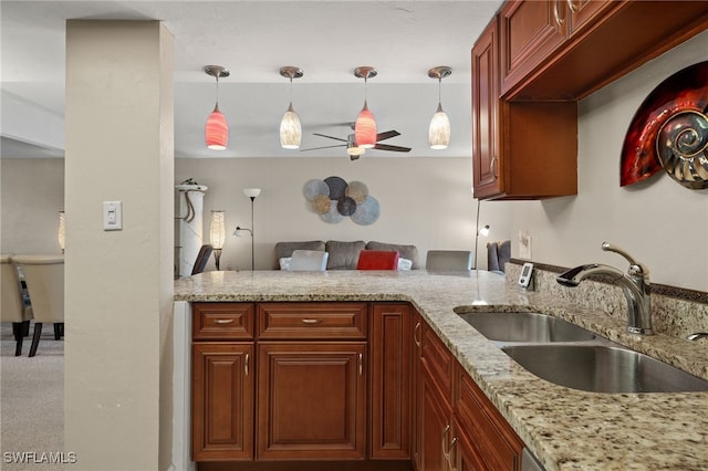 kitchen with kitchen peninsula, light stone counters, ceiling fan, sink, and pendant lighting