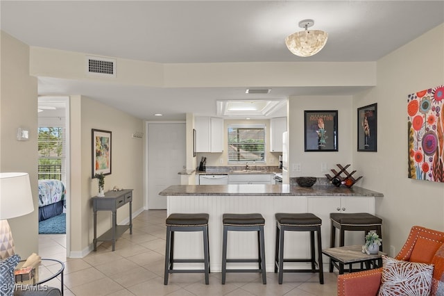 kitchen with kitchen peninsula, a breakfast bar, sink, light tile patterned floors, and white cabinets