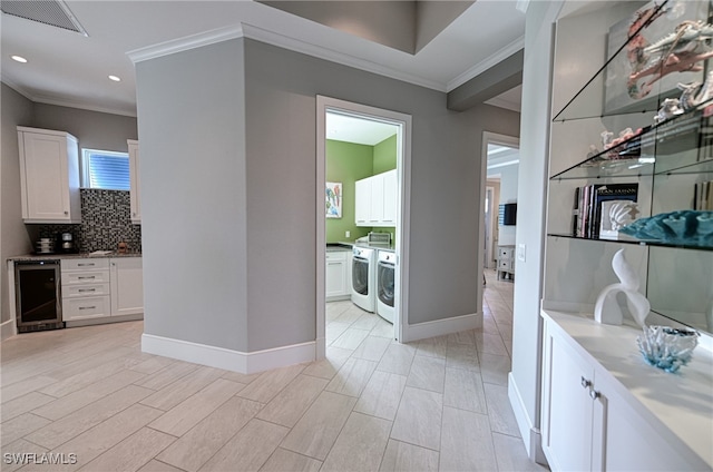 corridor with light wood-type flooring, washing machine and dryer, wine cooler, and ornamental molding