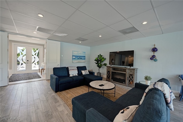 living room featuring a fireplace, french doors, light wood-type flooring, and a paneled ceiling