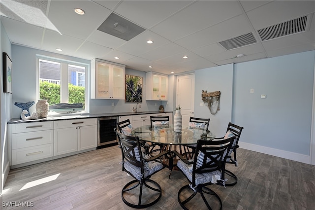 dining room with a drop ceiling, sink, beverage cooler, and light wood-type flooring