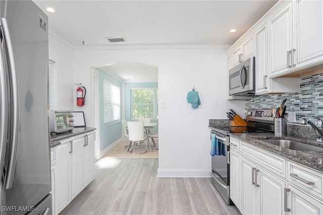 kitchen with stainless steel appliances, sink, dark stone countertops, light hardwood / wood-style floors, and white cabinetry