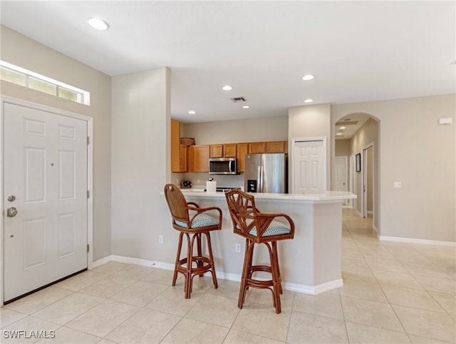 kitchen with kitchen peninsula, light tile patterned floors, a kitchen bar, and stainless steel appliances