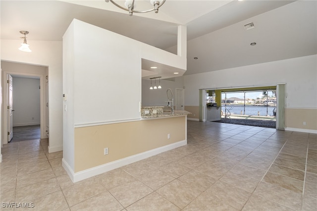 unfurnished living room with light tile patterned floors, high vaulted ceiling, a water view, and an inviting chandelier