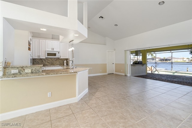 kitchen with kitchen peninsula, light stone counters, decorative light fixtures, a water view, and white cabinetry