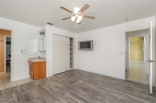 unfurnished bedroom featuring ceiling fan, a closet, light hardwood / wood-style floors, and sink