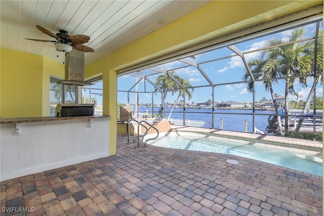 view of pool with ceiling fan, a bar, a water view, glass enclosure, and a patio area