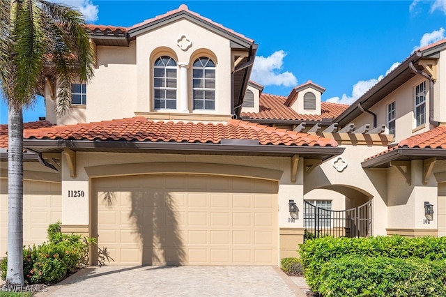 mediterranean / spanish-style house with an attached garage, a tiled roof, decorative driveway, and stucco siding