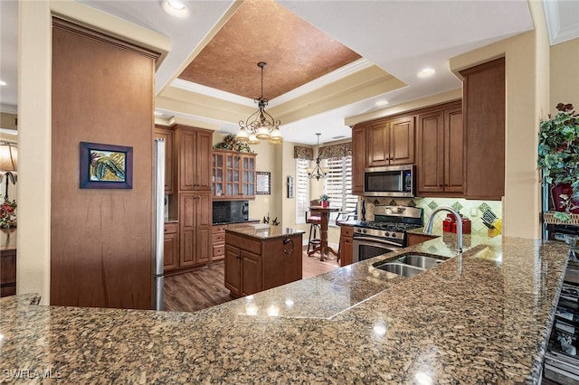 kitchen featuring wood finished floors, a sink, appliances with stainless steel finishes, brown cabinets, and a tray ceiling