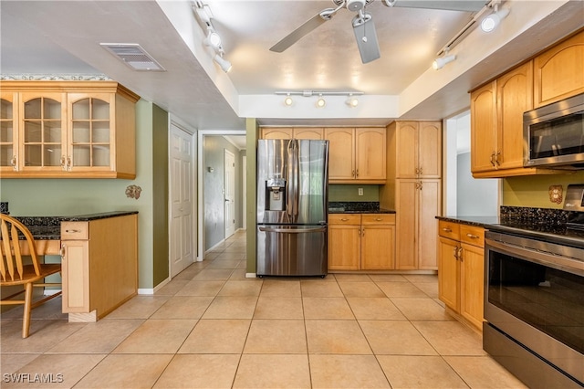 kitchen with light tile patterned flooring, dark stone countertops, stainless steel appliances, and track lighting