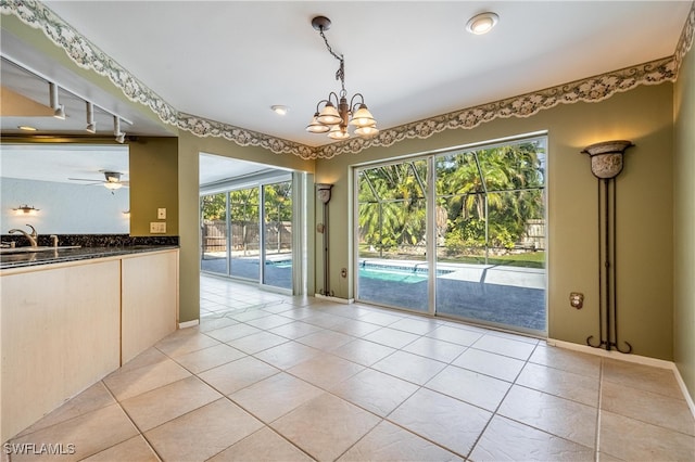 unfurnished dining area featuring ceiling fan with notable chandelier, sink, light tile patterned floors, and rail lighting