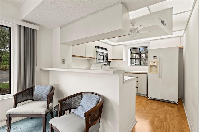 kitchen featuring white cabinetry, kitchen peninsula, ceiling fan, white fridge with ice dispenser, and a textured ceiling