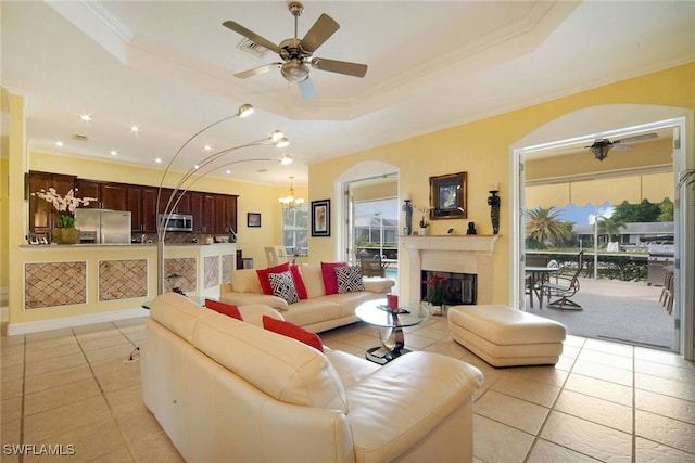 tiled living room with ceiling fan with notable chandelier, a raised ceiling, and ornamental molding