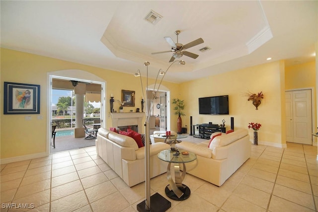 living room with ornamental molding, ceiling fan, a tray ceiling, and light tile patterned floors