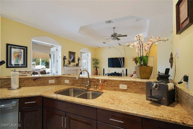 kitchen with light stone countertops, sink, ceiling fan, a tray ceiling, and dark brown cabinets